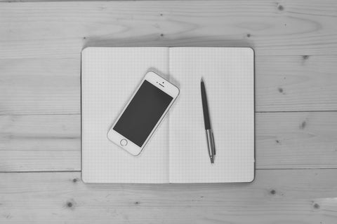 A smartphone and a pen lying on an open notebook on a table