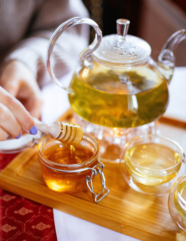 Someone dripping honey into a pretty glass jar on a wooden tray